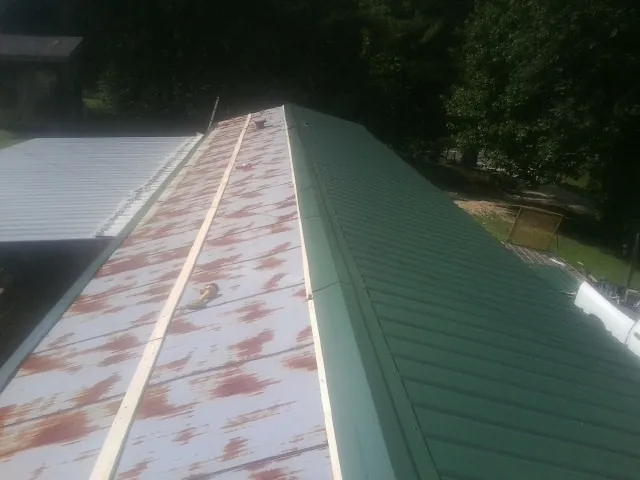 Old rusted panels beside newly installed green metal roofing in Chester